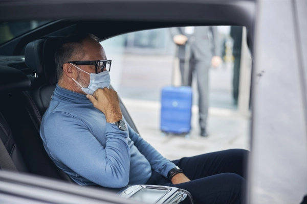 Mann mit Mund- und Nasenschutz sitzt im Taxi auf dem Weg zum Arzt.